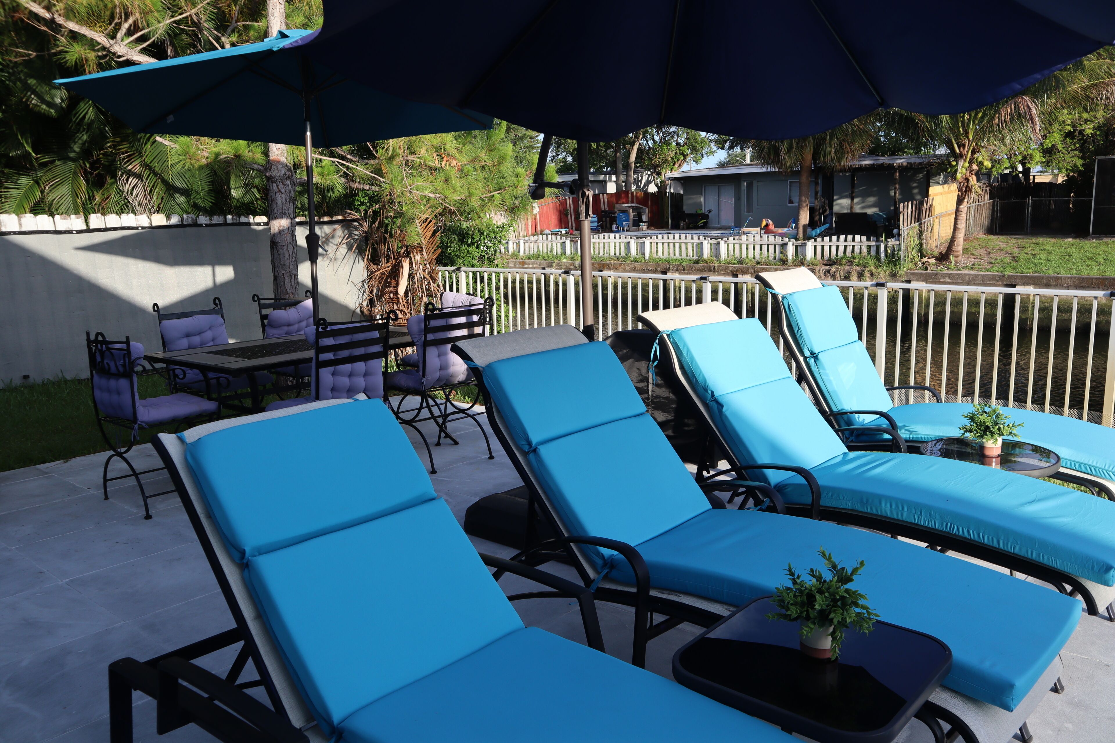 A patio with blue lounge chairs, a table, and umbrellas.