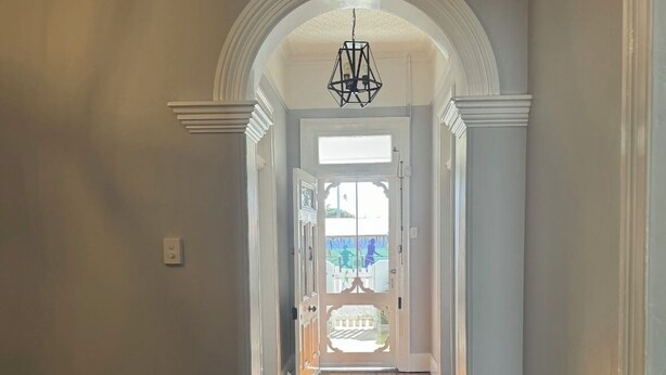 A hallway with wooden flooring, white walls, and an arched doorway leading to a bright room with a view.