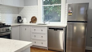 A modern kitchen with white cabinetry, a stainless steel refrigerator, a dishwasher, and a window with a view of greenery outside.