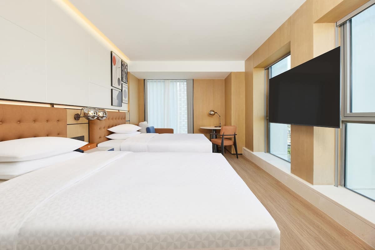 Habitación de hotel con tres camas, un escritorio y un ventanal grande.