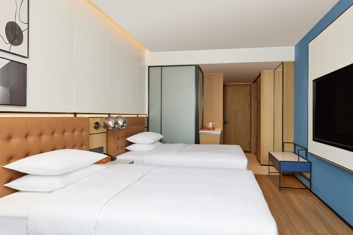 Habitación de hotel con dos camas, un televisor, una mesita de noche y un armario.