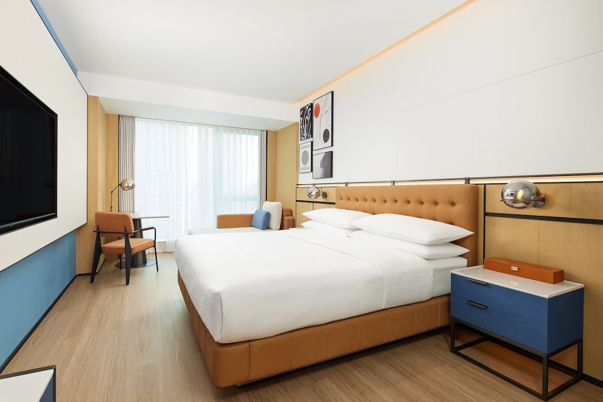 Una habitación de hotel moderna con una cama grande, un escritorio, una silla y un televisor.