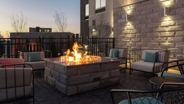 An outdoor seating area with a stone fire pit, lounge chairs, and a stone wall with lighting fixtures. - Fairfield By Marriott Inn & Suites Cincinnati Oakley (Cincinnati)