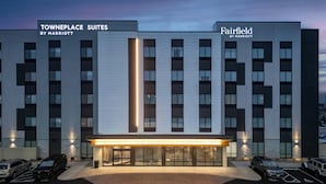 A modern hotel with two sections labeled Towneplace Suites and Fairfield by Marriott. It features a central entrance with a lighted pathway and a parking area with several cars. - Fairfield By Marriott Inn & Suites Cincinnati Oakley (Cincinnati)