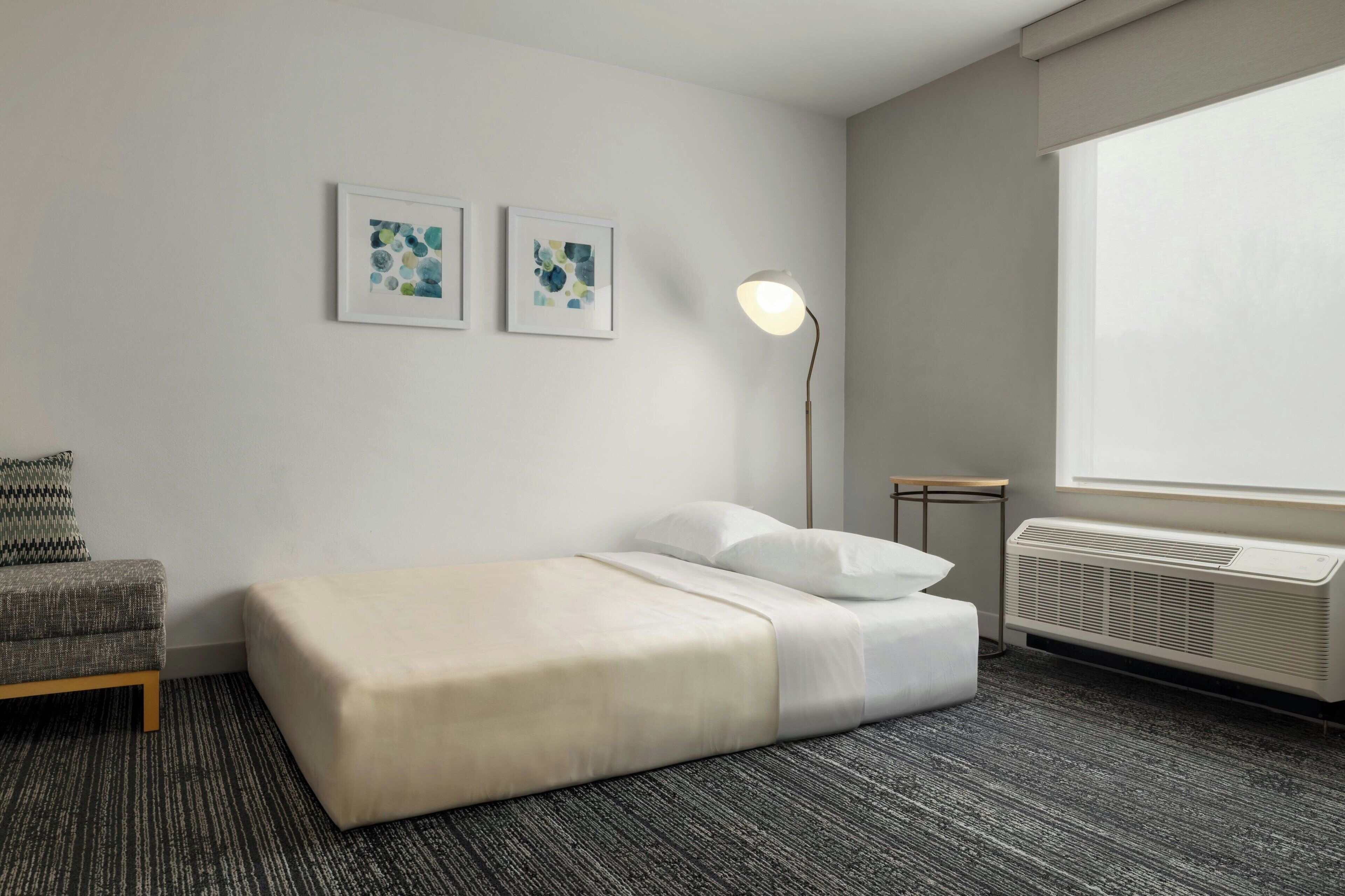 Een hotelkamer met een bed, een bureau, een stoel, een staande lamp en een raam.