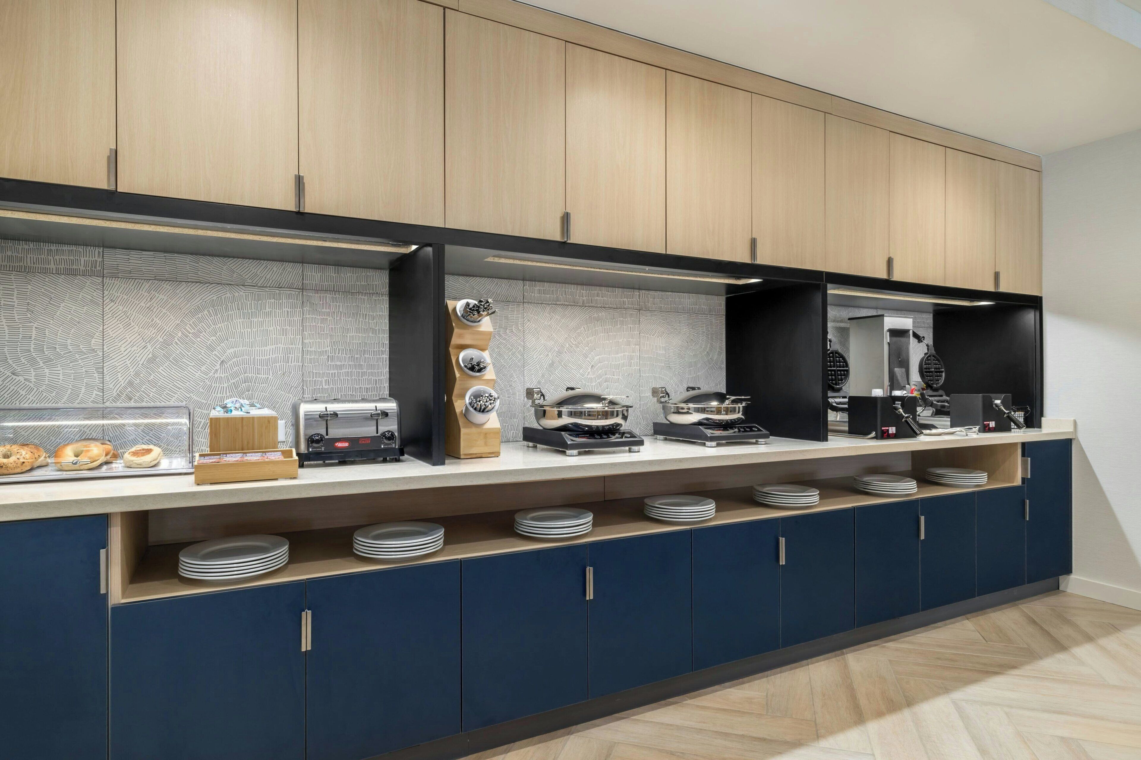 A modern kitchen with wooden cabinets, a countertop with various appliances, and a herringbone-patterned backsplash.