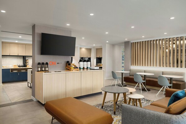 Un espacio moderno para estar, con cocina, televisor de pantalla plana y zona de asientos con mesas y sillas.