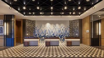 A modern hotel lobby with a geometric patterned floor, a central reception desk, and a ceiling with a unique light fixture design.