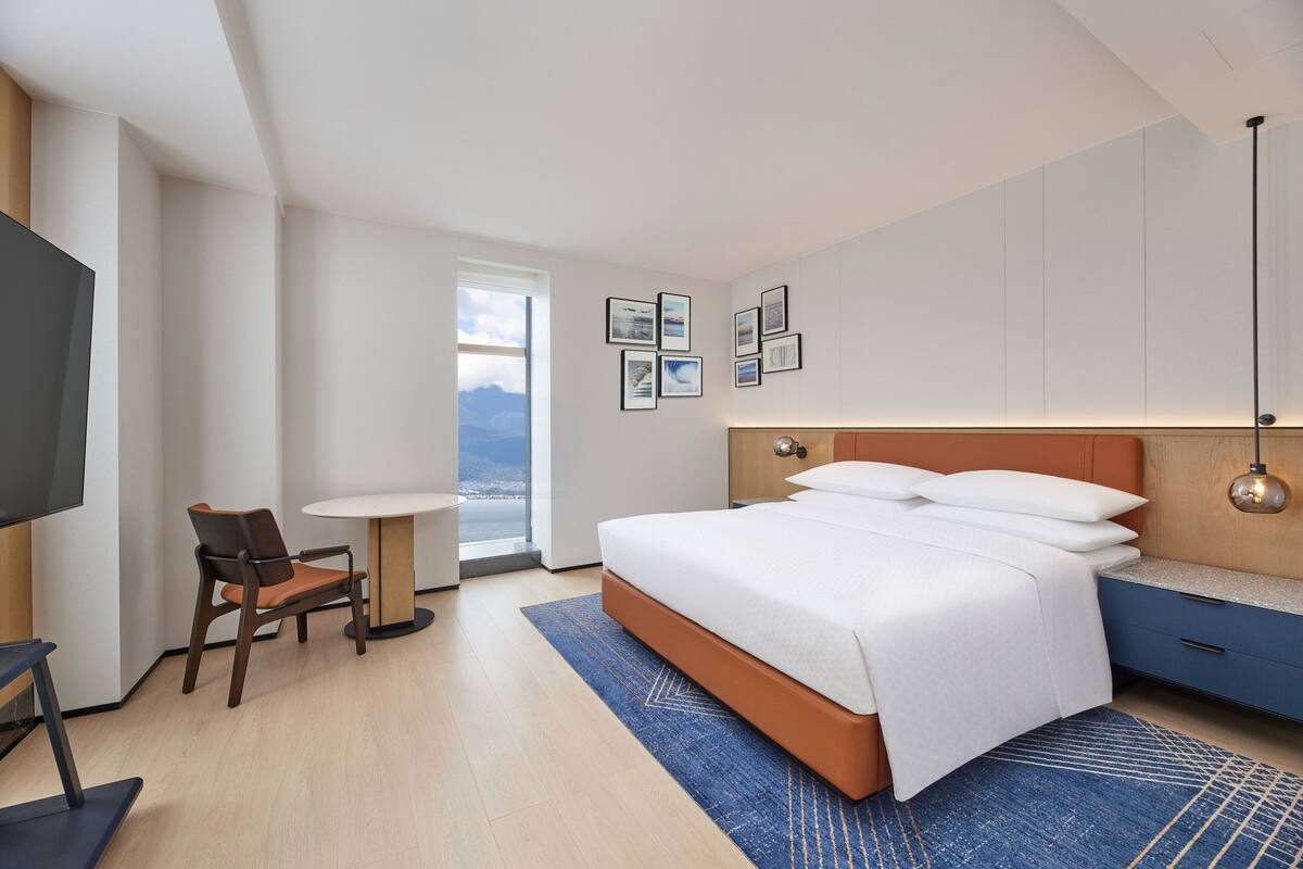 A modern hotel room with a large bed, a desk, and a television.