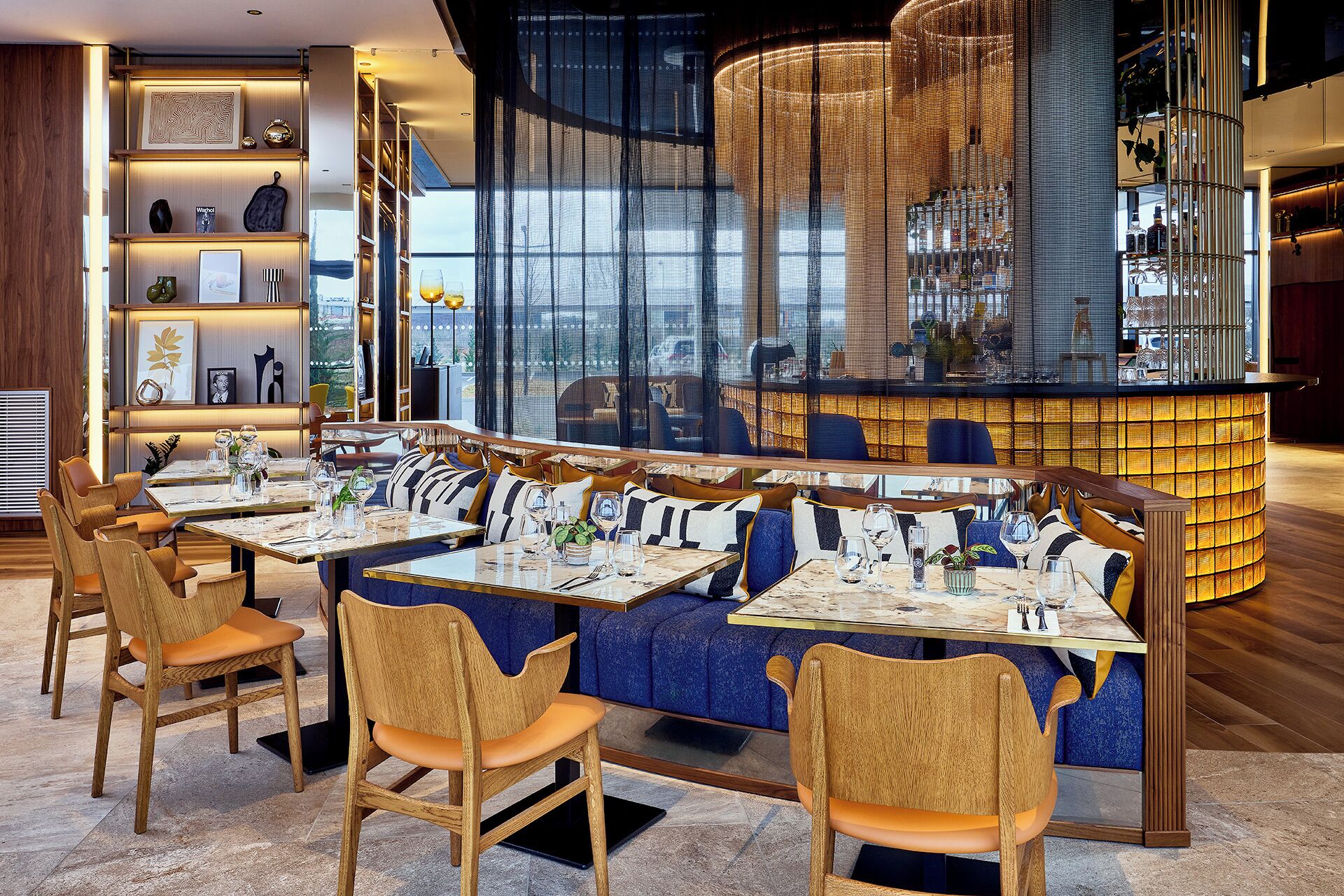 A modern restaurant with a bar area, wooden chairs, and a view through a large window.