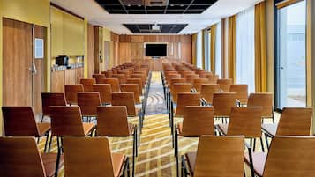 Un salón de conferencias con filas de sillas, una pantalla grande y suelo alfombrado.