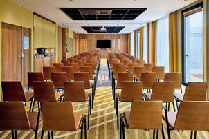Un salón de conferencias con filas de sillas, una pantalla grande y suelo alfombrado.