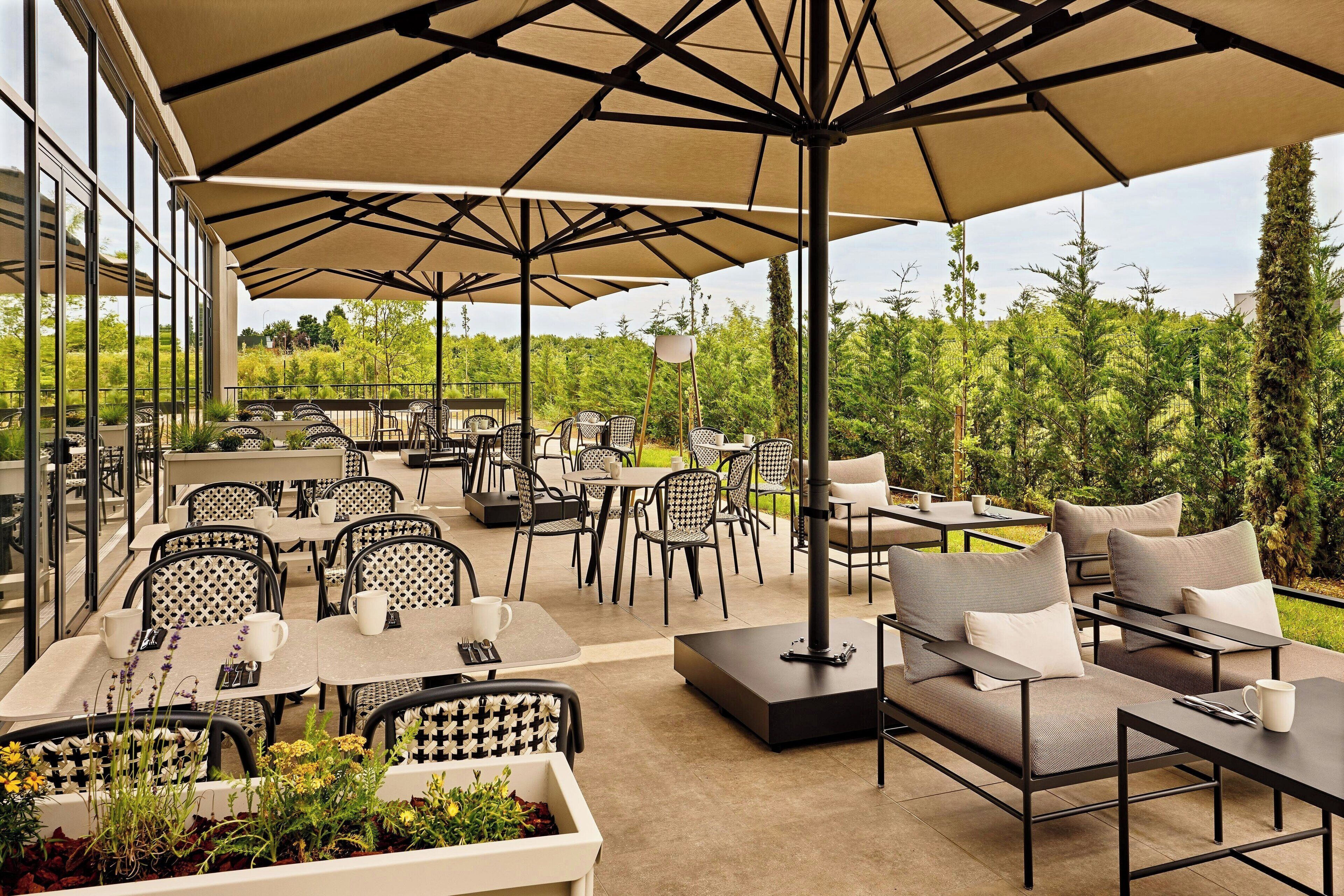 An outdoor patio with tables and chairs, large umbrellas, and a view of greenery.