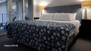 Hotellihuone, jossa on Galaxy A55 5G -mallin teemalla sisustettu sänky, tumma pääty, kaksi yöpöytävalaisinta ja näkymä ulkopuolella olevalle parvekkeelle.