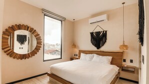 Ein modernes Schlafzimmer mit einem großen Bett, einem runden Spiegel, einer Pendelleuchte und Blick durch ein Fenster.