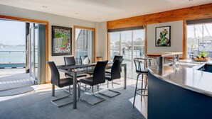 A modern kitchen with a large island, a dining area with a table and chairs, and large windows offering a view of the water.