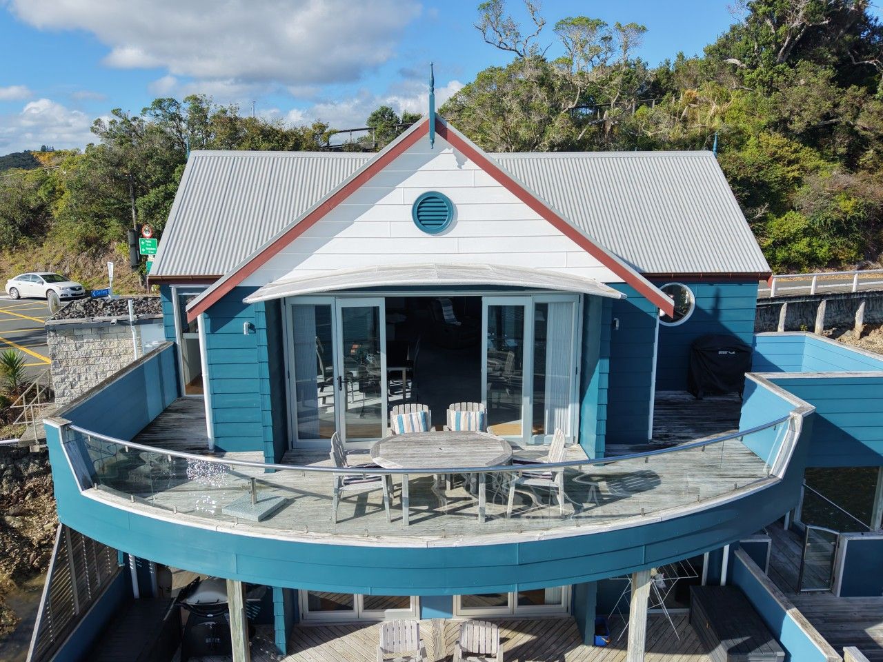 Una propiedad frente al agua con una terraza curva, un área de comedor con mobiliario exterior y un edificio con techo rojo.