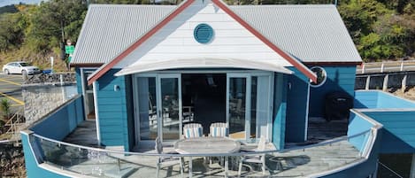 Una propiedad frente al agua con una terraza curva, un área de comedor con mobiliario exterior y un edificio con techo rojo.
