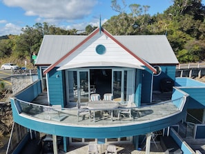 Une propriété située au bord de l’eau, dotée d’une terrasse incurvée, d’un espace repas avec mobilier d’extérieur et d’un bâtiment avec un toit rouge.