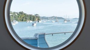 Ein rundes Fenster mit Blick auf einen Hafen, Boote und eine ferne Küstenlinie.
