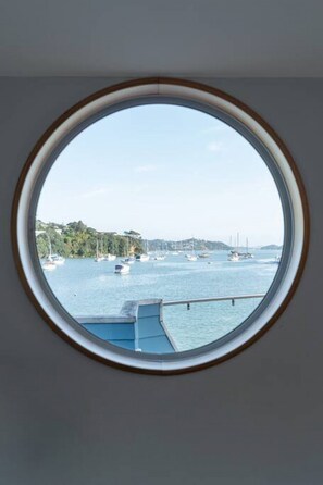 Una ventana redonda con vista a un puerto, barcos y una costa lejana.