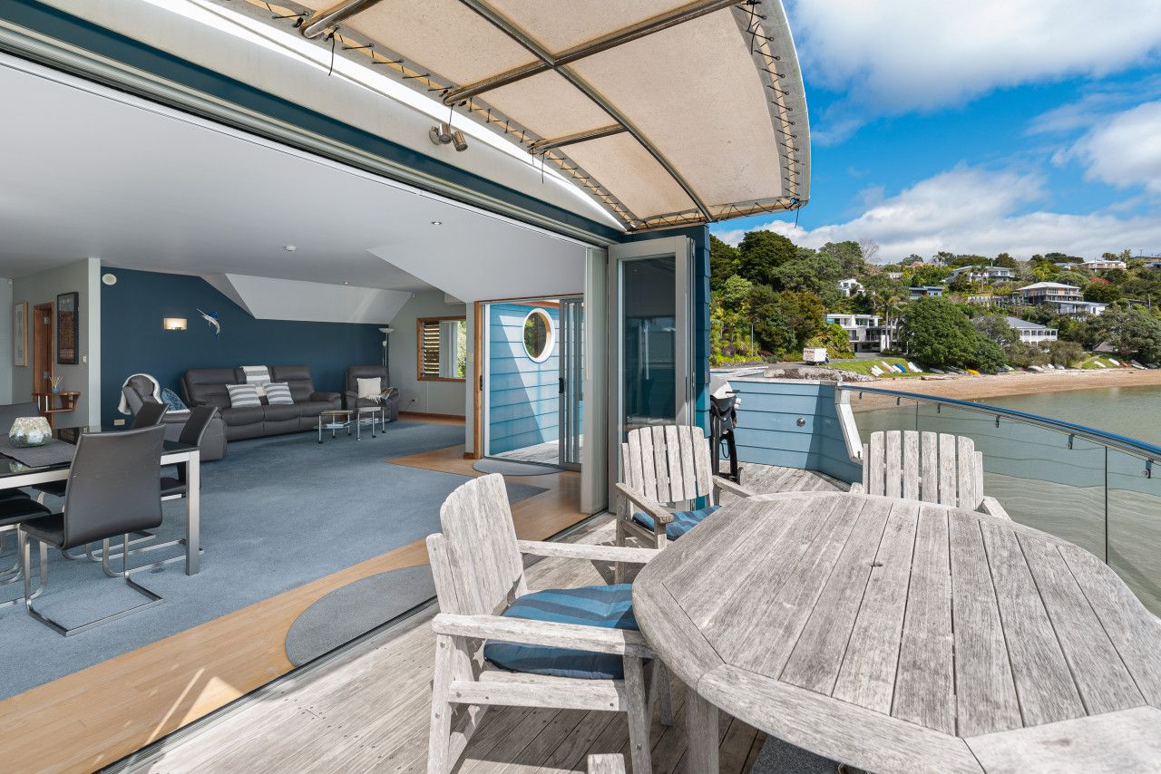 A sunlit outdoor deck with a round wooden table and chairs, a sofa, and a dining area.