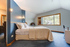 Un dormitorio con cama, escritorio, silla, ventana y vistas al exterior.