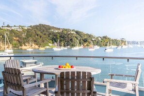 A deck with wooden chairs and a table, overlooking a marina with boats and a hilly landscape in the background.