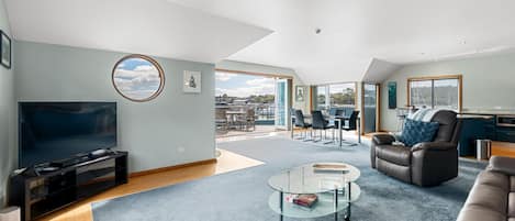 Een ruime woonkamer met een flatscreen televisie, een glazen salontafel en een comfortabele bank.