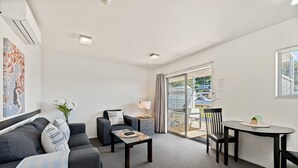 Una sala de estar moderna con un sofá gris, una mesita y una silla. Hay un ventanal corredero que da a un espacio exterior.