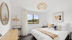 Une chambre avec un grand lit, un bureau en bois, un luminaire suspendu, une fenêtre avec vue et une œuvre d’art encadrée au mur.