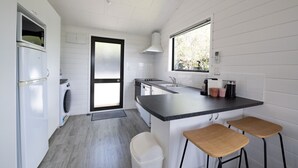 Une cuisine compacte avec des meubles blancs, un four encastré, un lave-linge, un évier et une fenêtre qui laisse entrer la lumière naturelle.