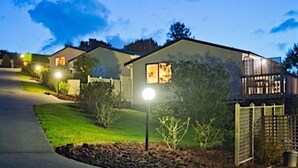 Un quartier résidentiel au crépuscule, avec des maisons, une rue bien éclairée et un ciel dégagé.