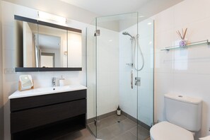 A modern bathroom with a glass-enclosed shower, a white sink with a mirror, and a toilet. - Paihia 2 Bdrm Apartment and Pool (Paihia)