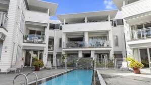 Un edificio moderno de varios pisos con piscina central, balcones y plantas en macetas.