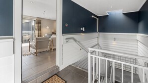 Un interior moderno con una escalera, un área de estar con un sofá y una mesa de centro, y vistas al exterior.