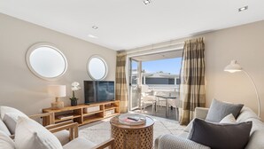 Una sala de estar moderna con televisor, sofá y mesa de centro. Hay un balc ón con vistas a la ciudad.