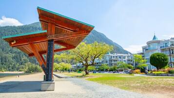 A wooden pavilion with a green roof in a park with a mountain backdrop and modern buildings.