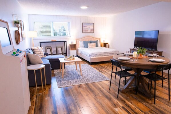 A modern, well-lit room with a bed, sofa, dining table, and TV.