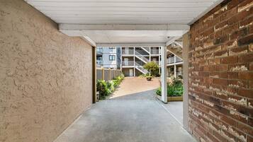 A corridor with a concrete floor, a brick wall on the right, and a building with balconies in the background.