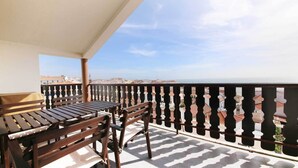 Un balcón con mesa y sillas de madera, piso con diseño y vista a edificios y al mar.