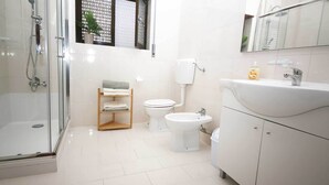 Un baño moderno con ducha envuelta en vidrio, inodoro, bidé y lavamanos con espejo superior.