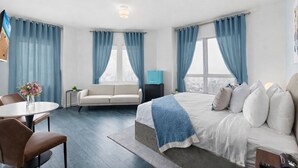 A modern hotel room with a large bed, a sofa, a dining table, and a view of the city. - Global Luxury Suites at The Apex Miami (Miami Beach)