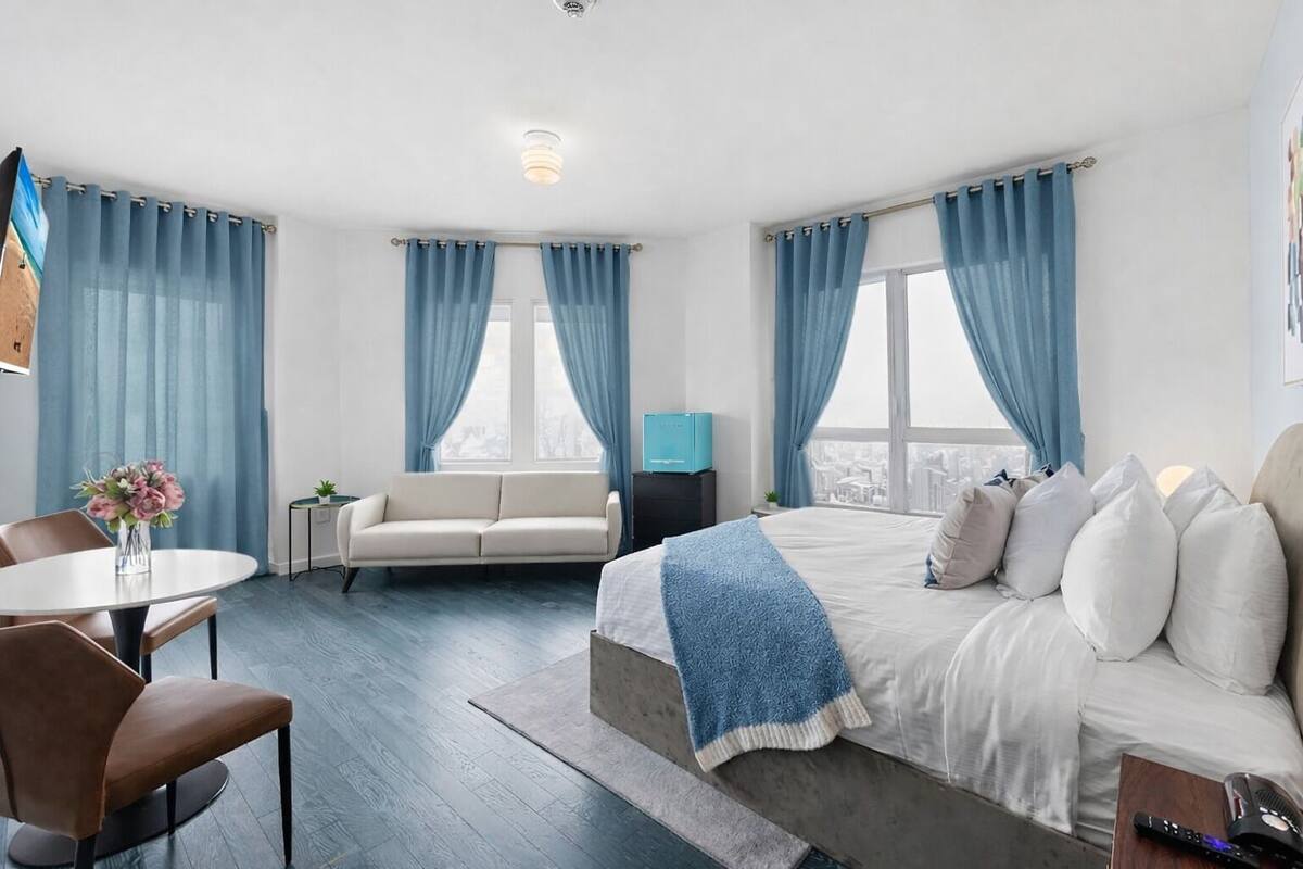 Habitació d'hotel moderna amb un llit gran, un sofà, una taula de dinar i vista a la ciutat.