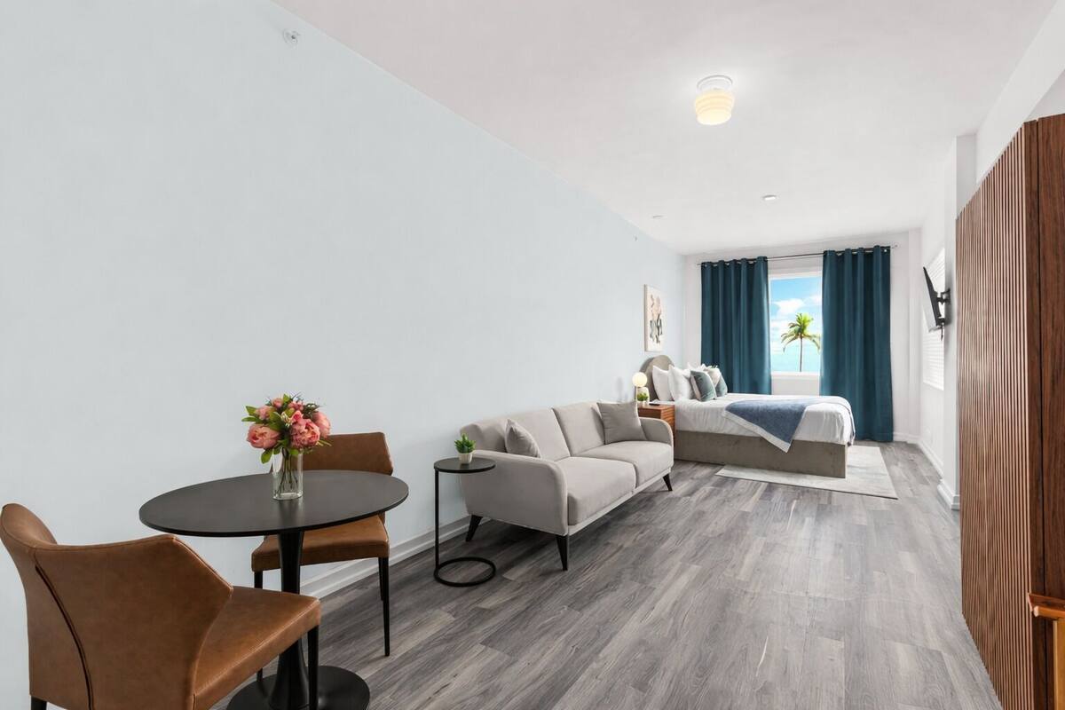 Un saló modern amb un sofà, una taula de menjador amb caires, una taula auxiliar petita i una finestra amb cortines.