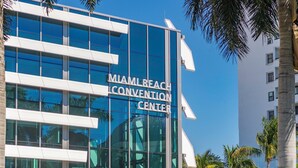 The Miami Beach Convention Center with a modern glass facade and palm trees in the background. - Global Luxury Suites at The Apex Miami (Miami Beach)