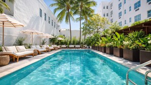 A pool area with lounge chairs and umbrellas, surrounded by greenery and modern buildings. - Global Luxury Suites at The Apex Miami (Miami Beach)