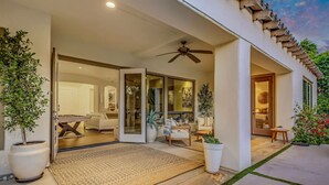 Ein modernes Haus mit einer überdachten Terrasse, großen Schiebetüren zu einem Wohnzimmer und einem Deckenventilator.