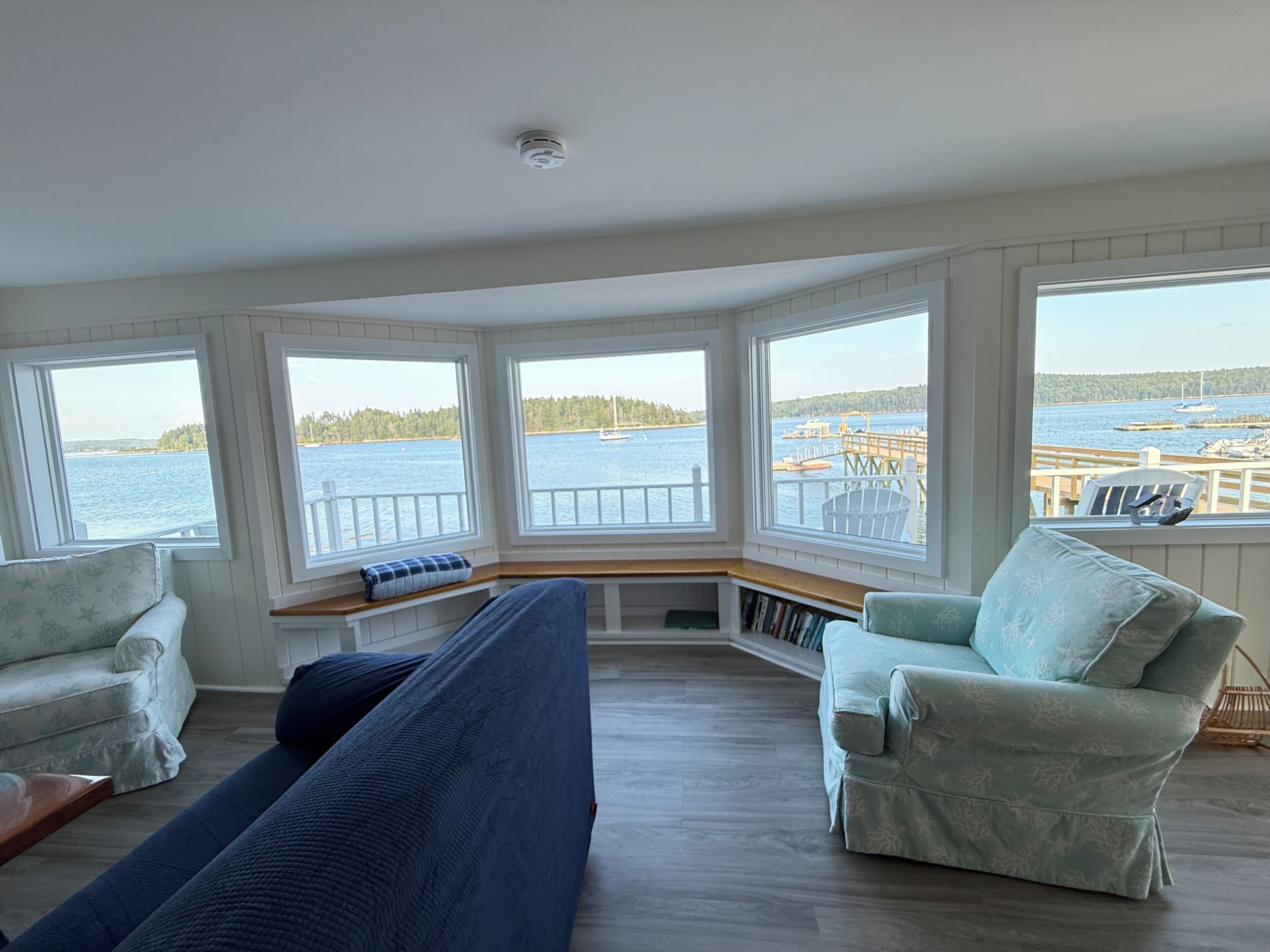 A room with a large bay window overlooking a body of water, a built-in bench, and two chairs.
