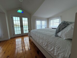 Une chambre avec un grand lit, une porte donnant sur un balcon et une fenêtre avec des rideaux.